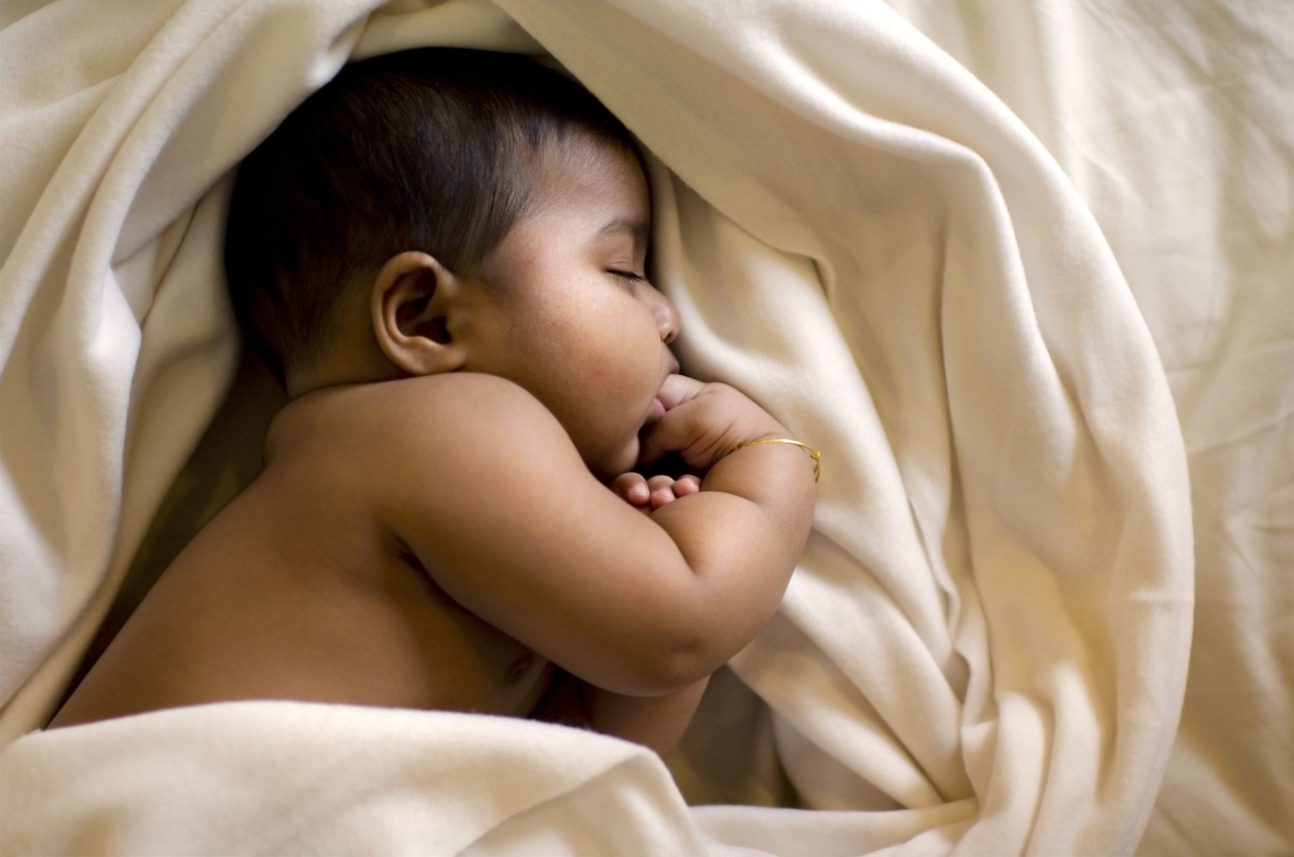 Muslim baby girl sleeping on her side in her crib.