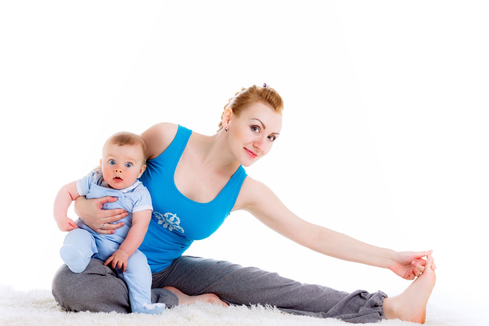 Young mother wears a post-pregnancy belt under her clothes as she stretches on an exercise mat with her baby.