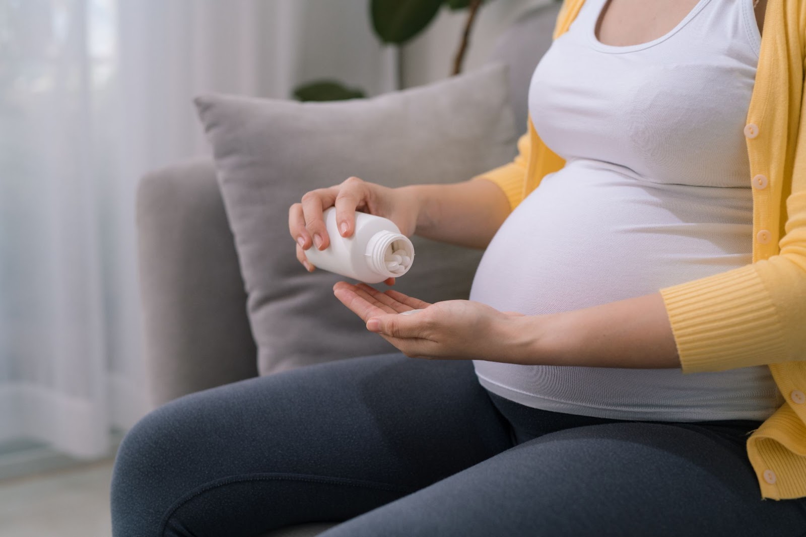 A pregnant woman sitting on a couch before taking an acetylcysteine tablet.